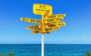 Colorful signpost at Bluff, New Zealand, showing global cities with ocean backdrop.
